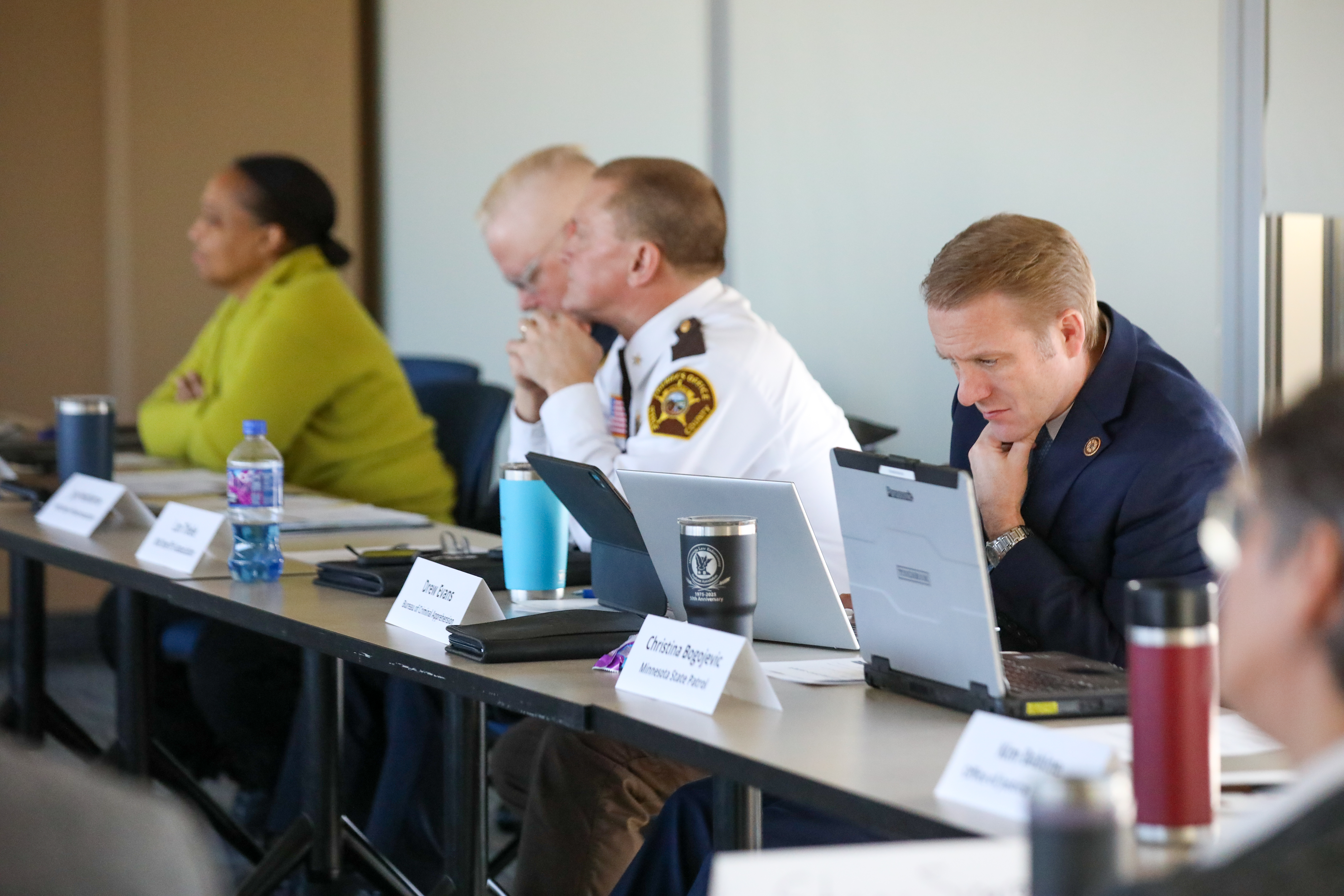 Members of the Governor's Statewide Safety Council sit at a table looking at laptops during a meeting.