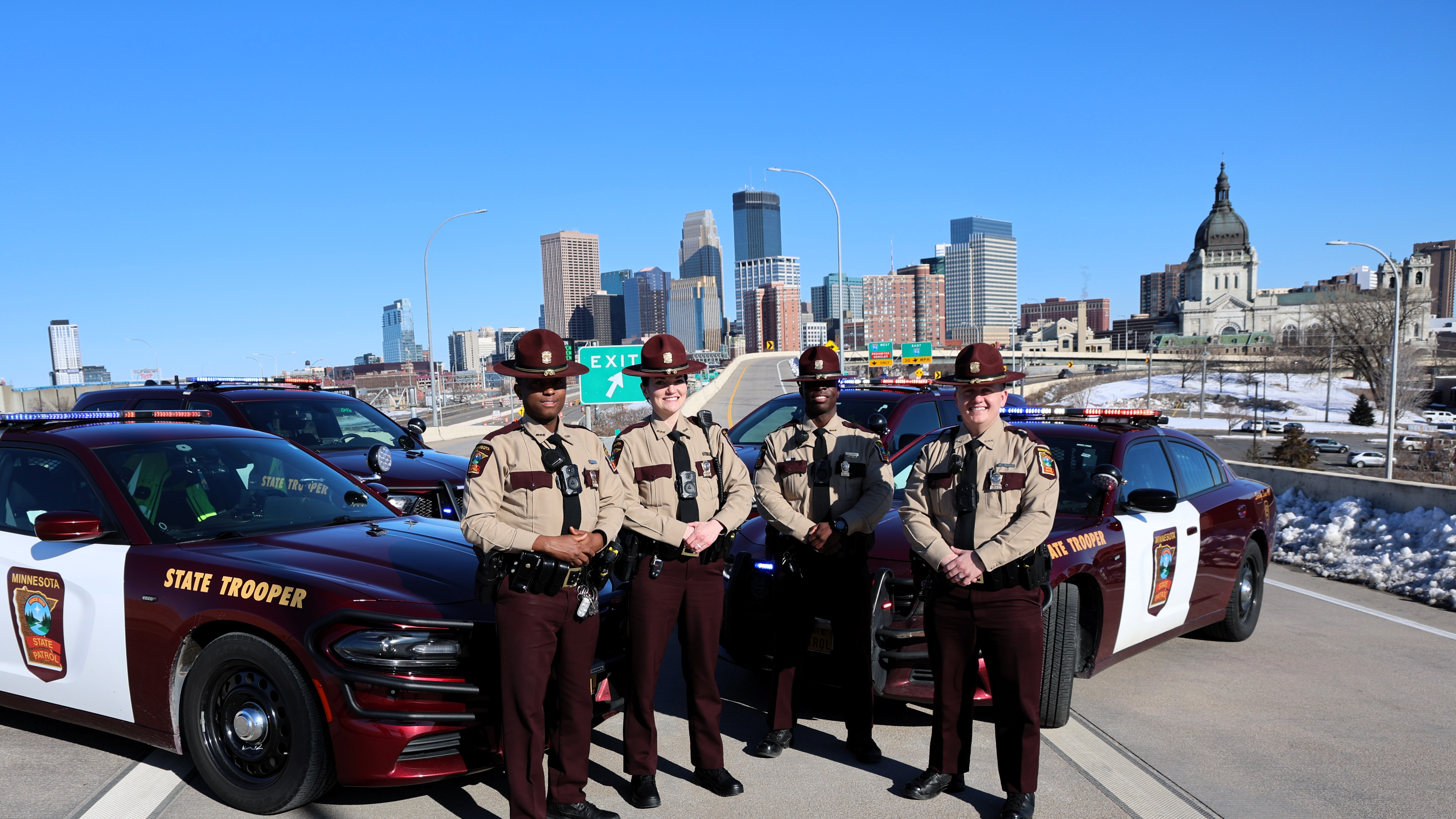 Image of four state troopers standing in front of squad cars