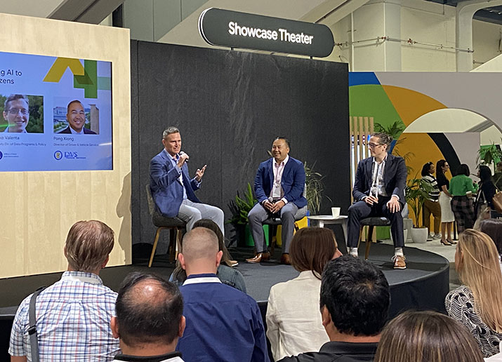 Three people on stage talking and seated audience members listening.