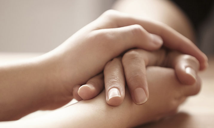 The hands of two people grasped on a tabletop. 