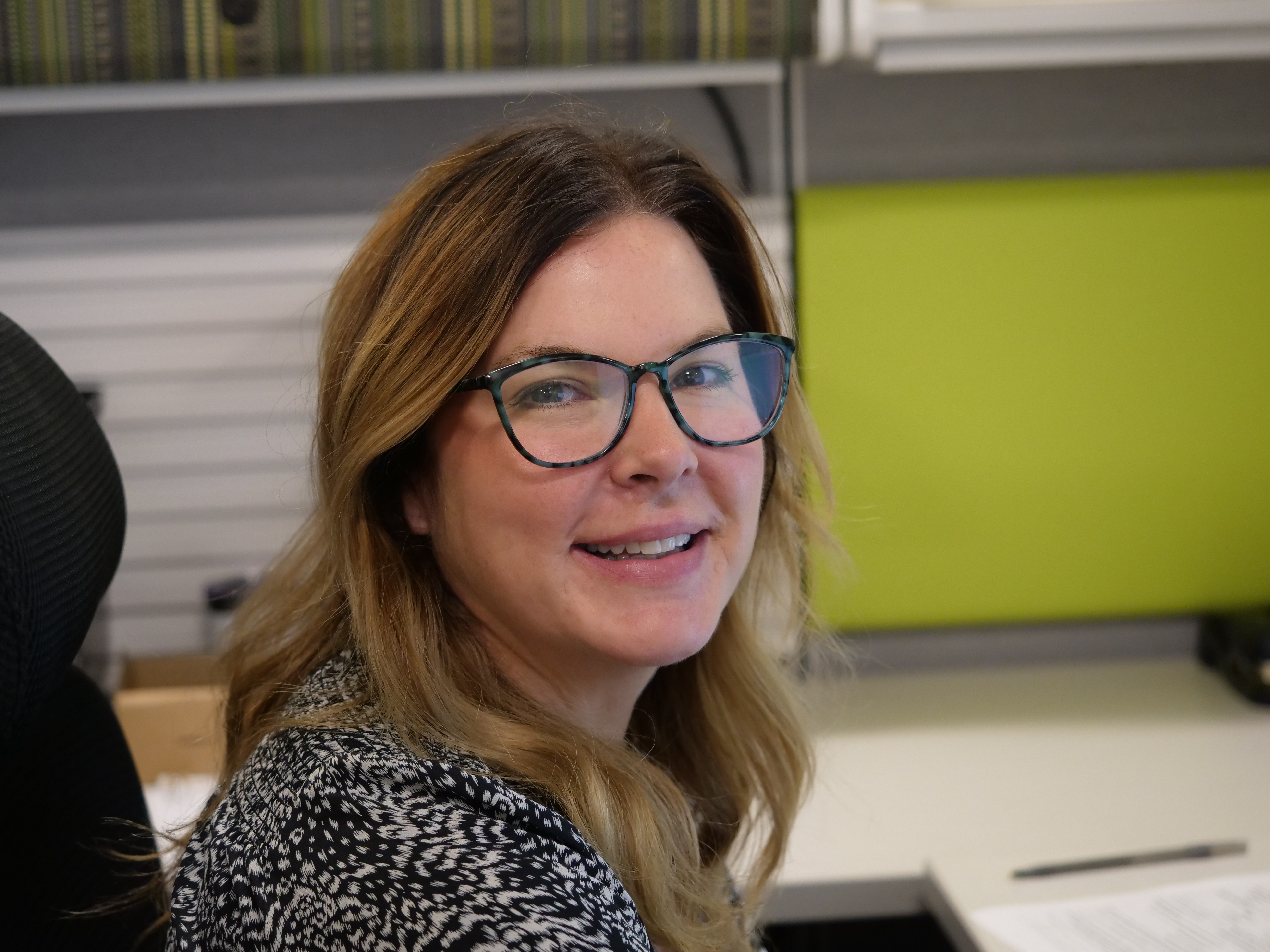 A DPS staff member smiling at the camera while sitting at her desk.