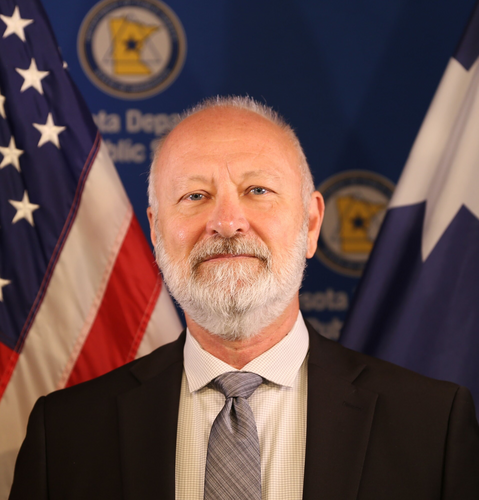 Commissioner Bob Jacobson in front of American and Minnesota state flags.