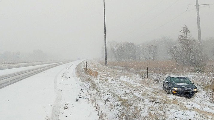 A car in the ditch alongside a snowy road.