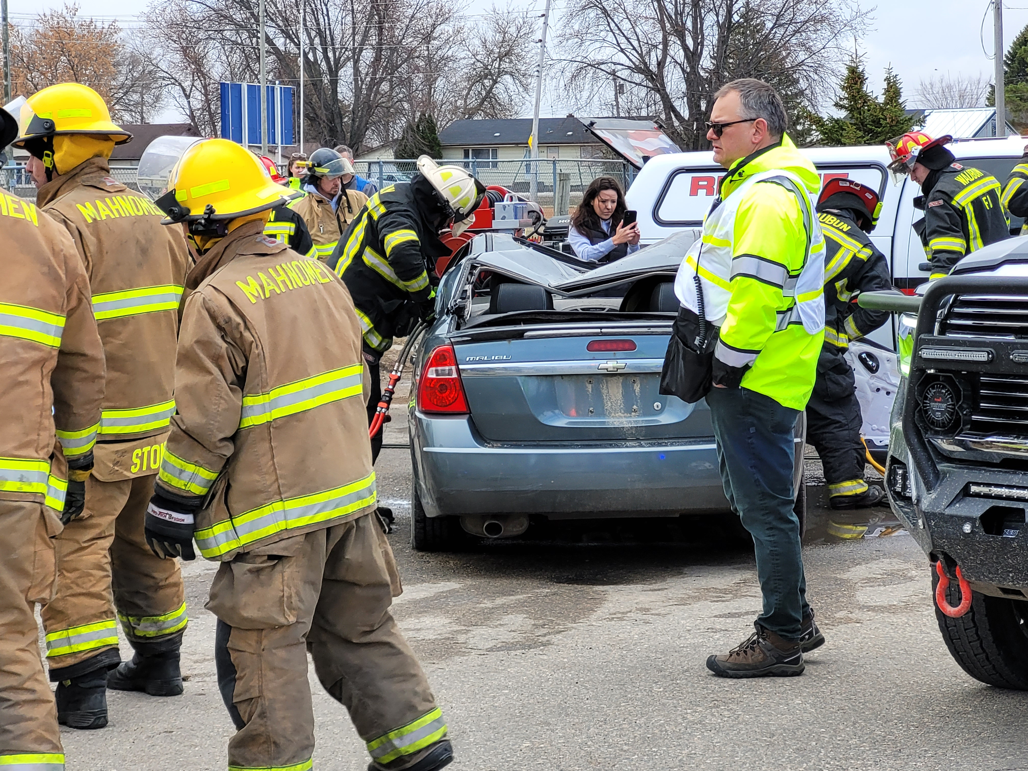 Firefighters and emergency manager Ed Snetsinger gathers at a crash. A car's hood is collapsed.