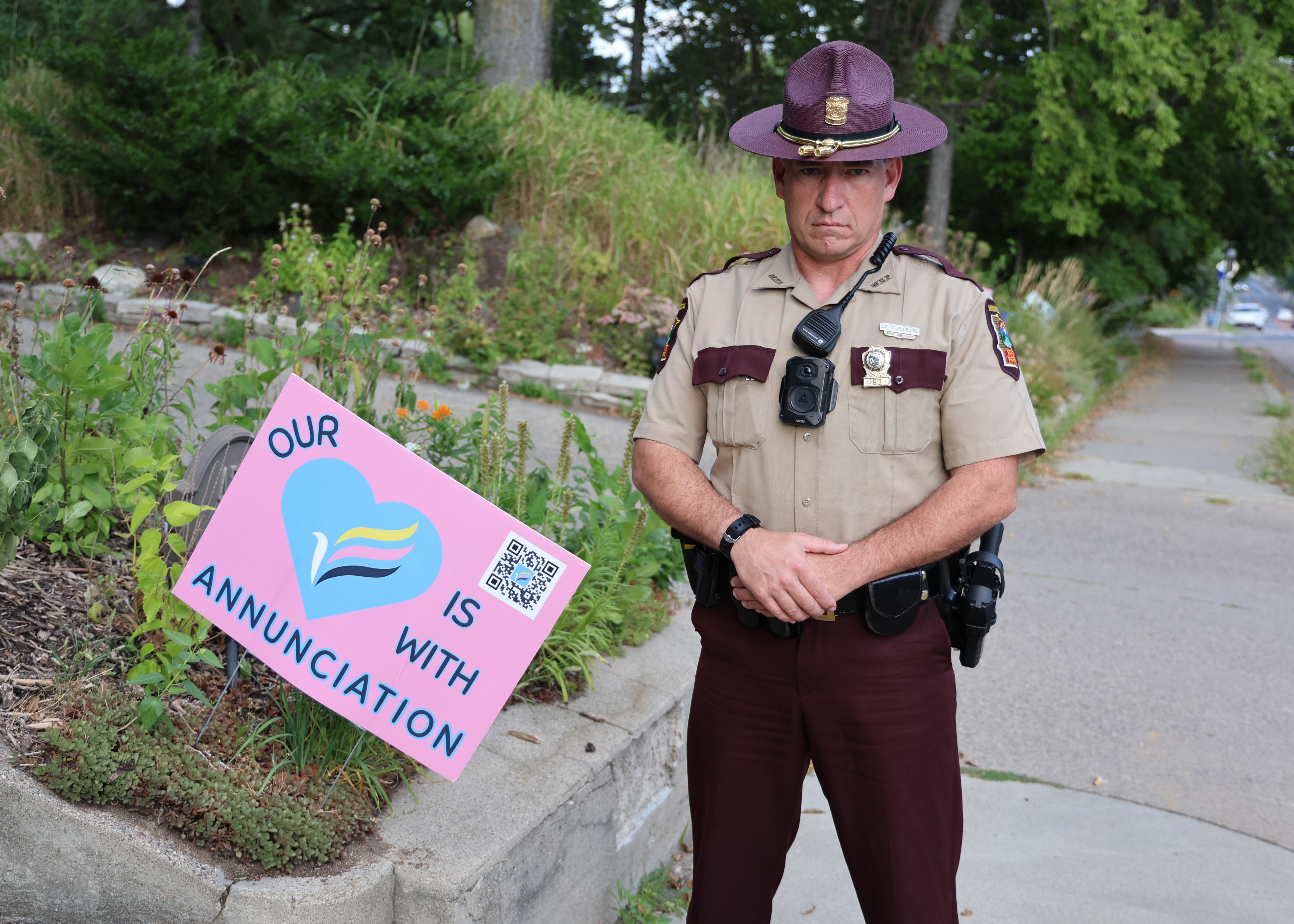 Trooper Eric Ouellette poses next to a sign that says our heart is with Annunciation