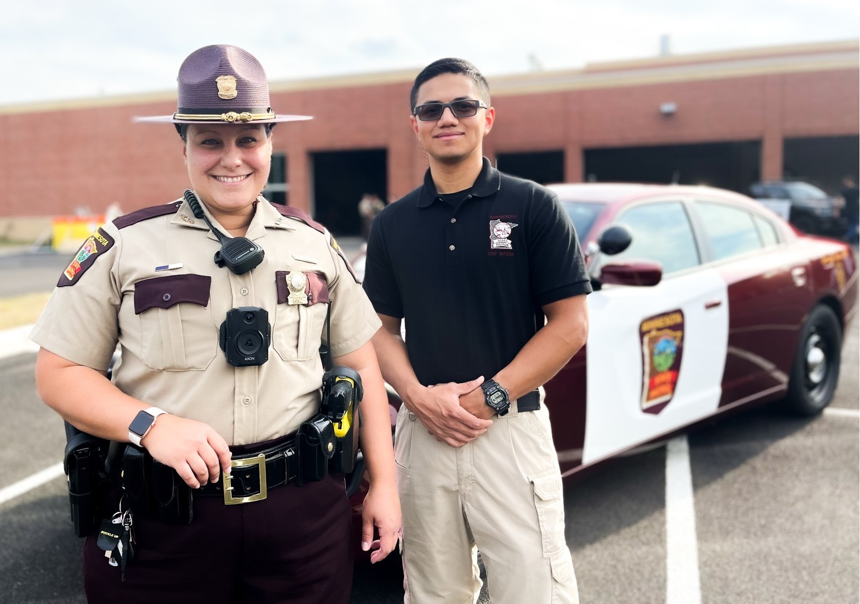 A Minnesota state trooper stands with an intern in front of a State Patrol vehicle