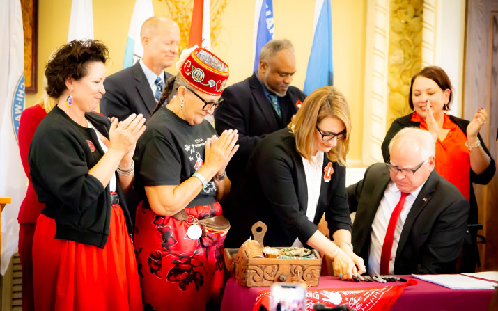 Gov. Tim Walz signs legislation creating the MMIW Task Force as supporters look on.
