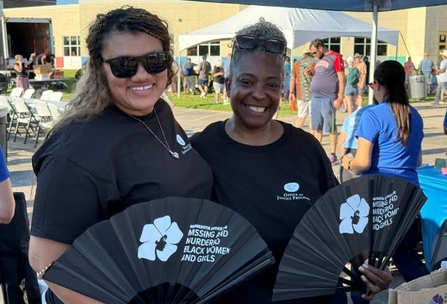 Two employees from the Office for Missing and Murdered Black Women and Girls holding fans outside at an event