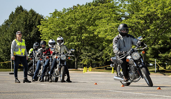 A motorcyclist navigating a training course as other riders watch.