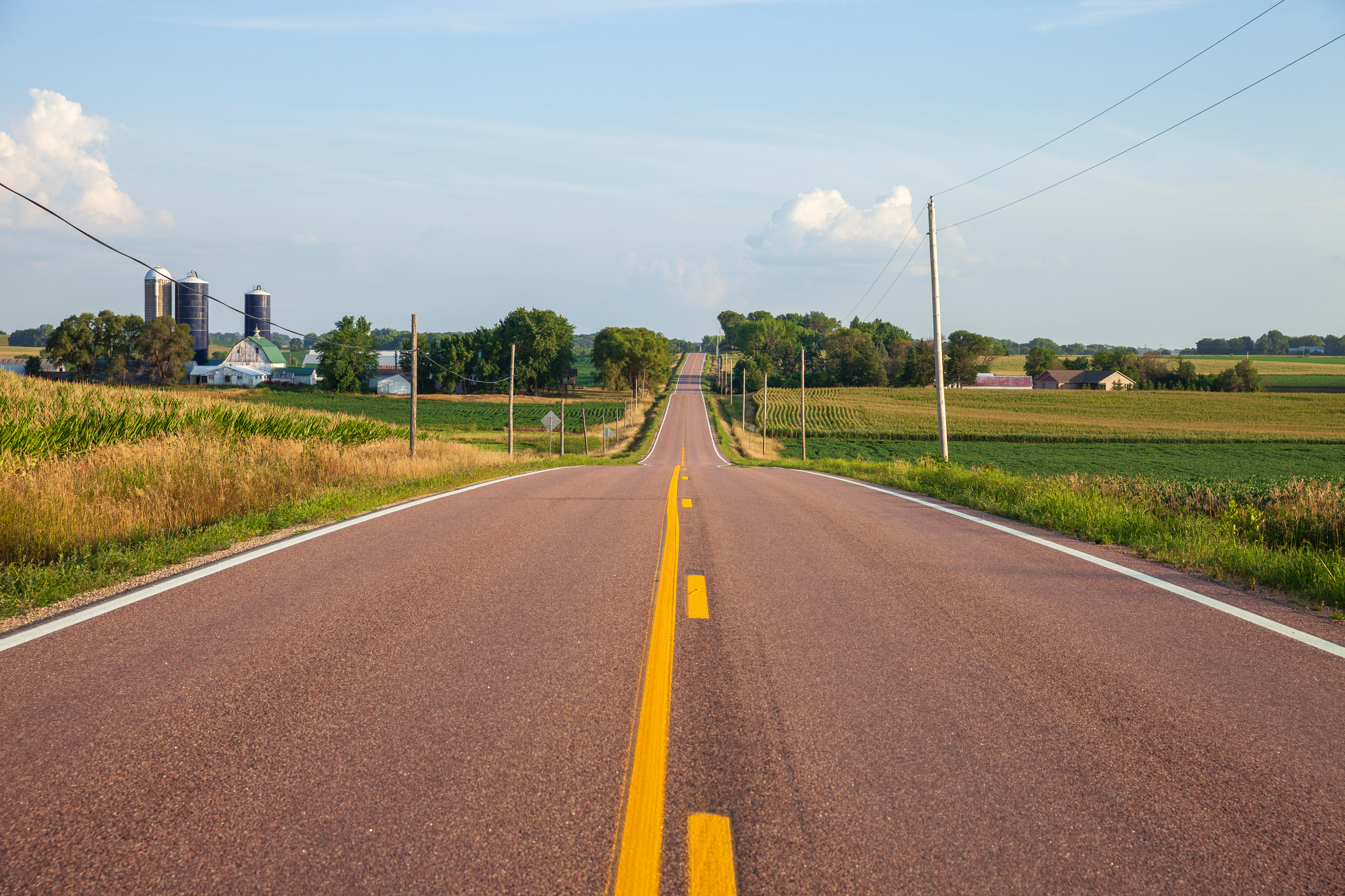 Rural two-lane road, farmstead on left side, farmland on right side of road