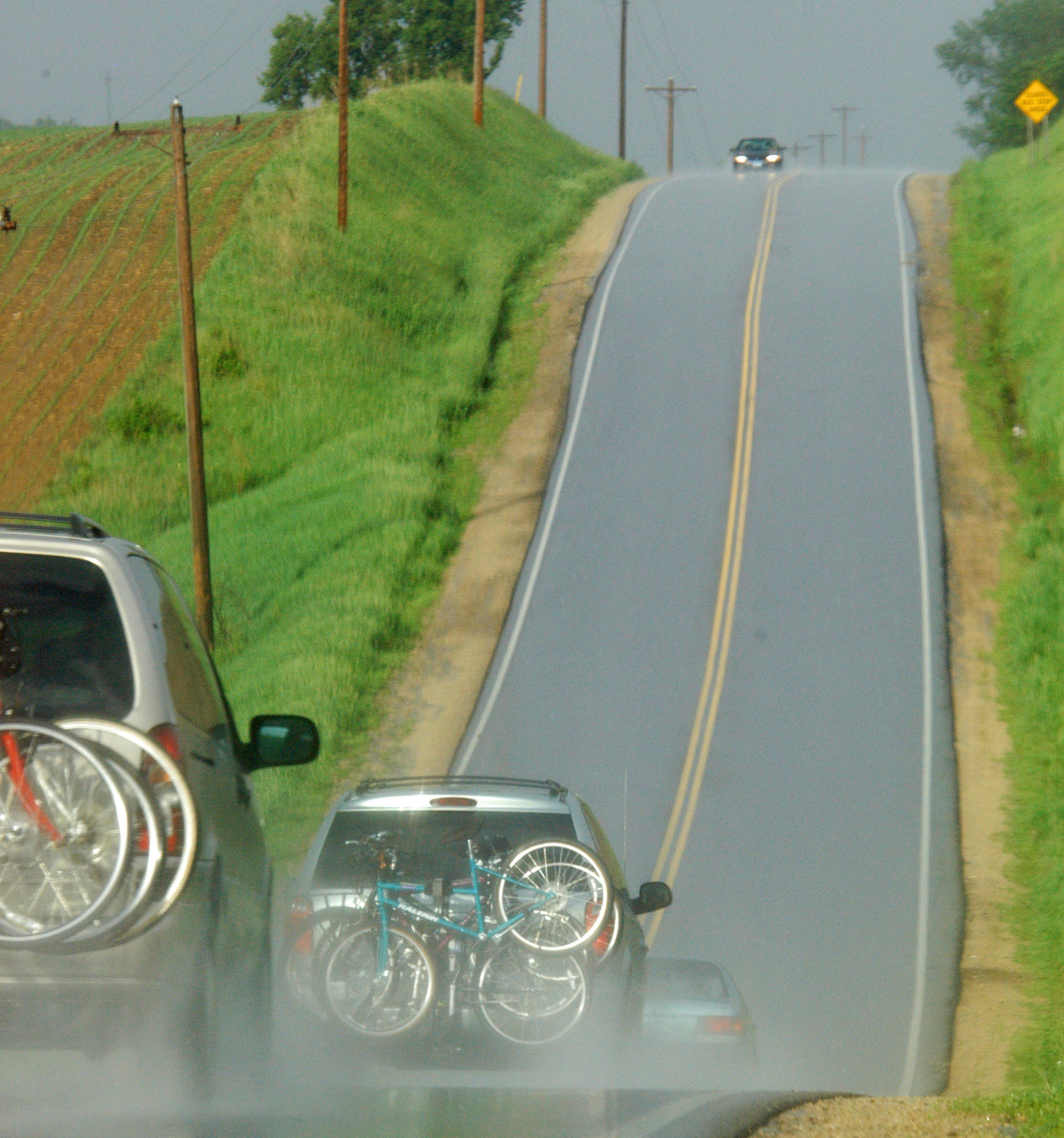 Cars with bicycles on the back driving on a wet rural highway