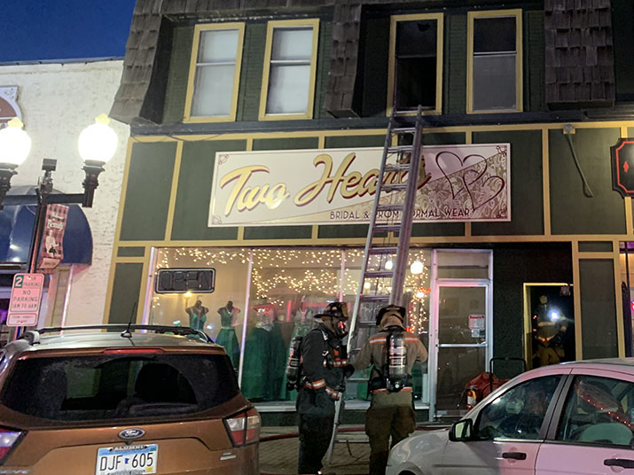 Two firefighters standing by a ladder going up to second-floor window.