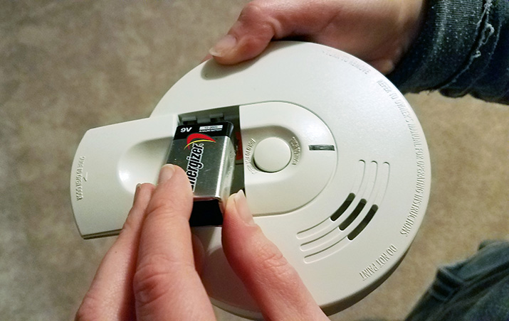 Hands place a battery inside a smoke alarm