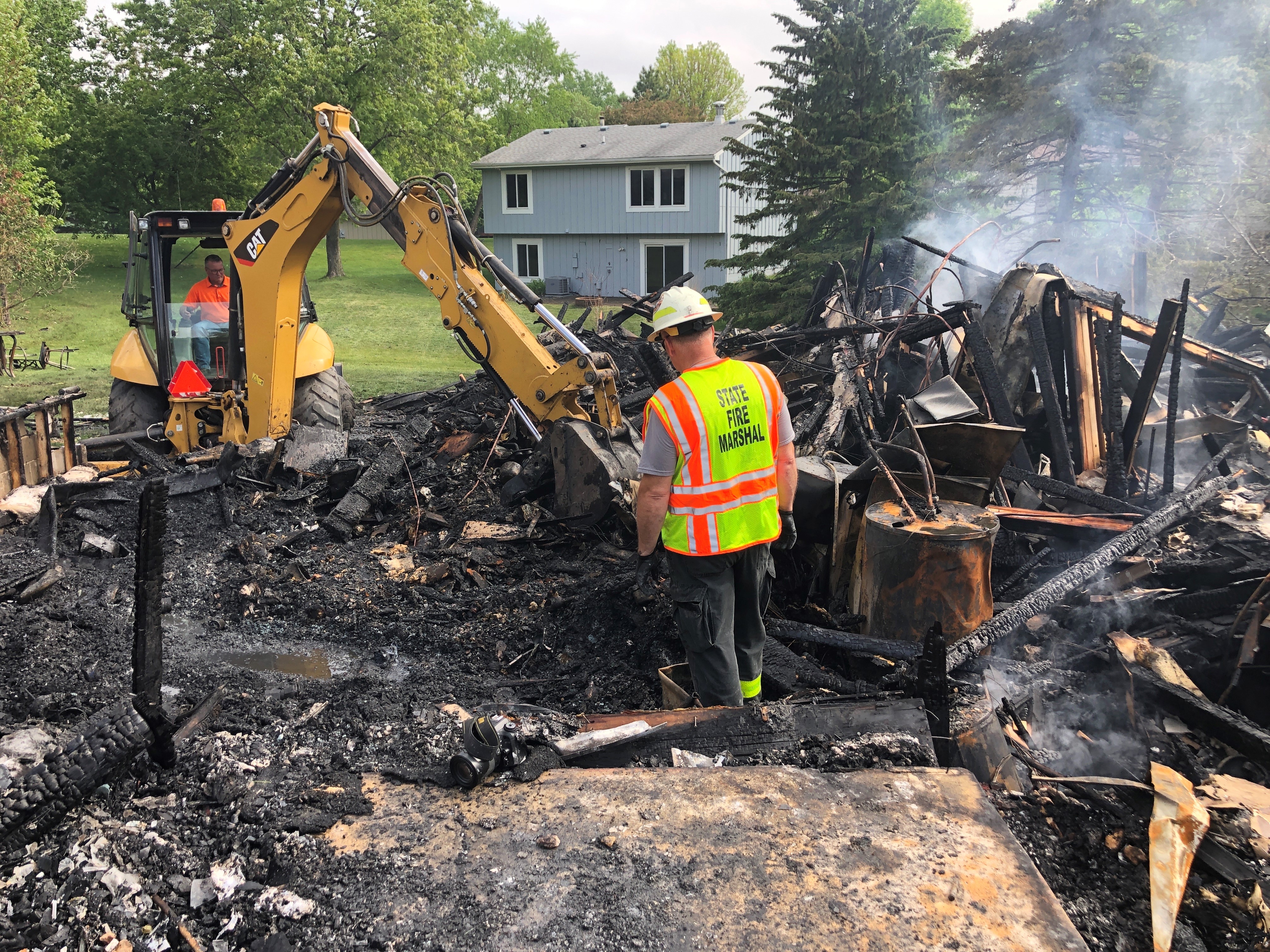 A State Fire Marshal investigator digs through smoking rubble at a fire scene. 