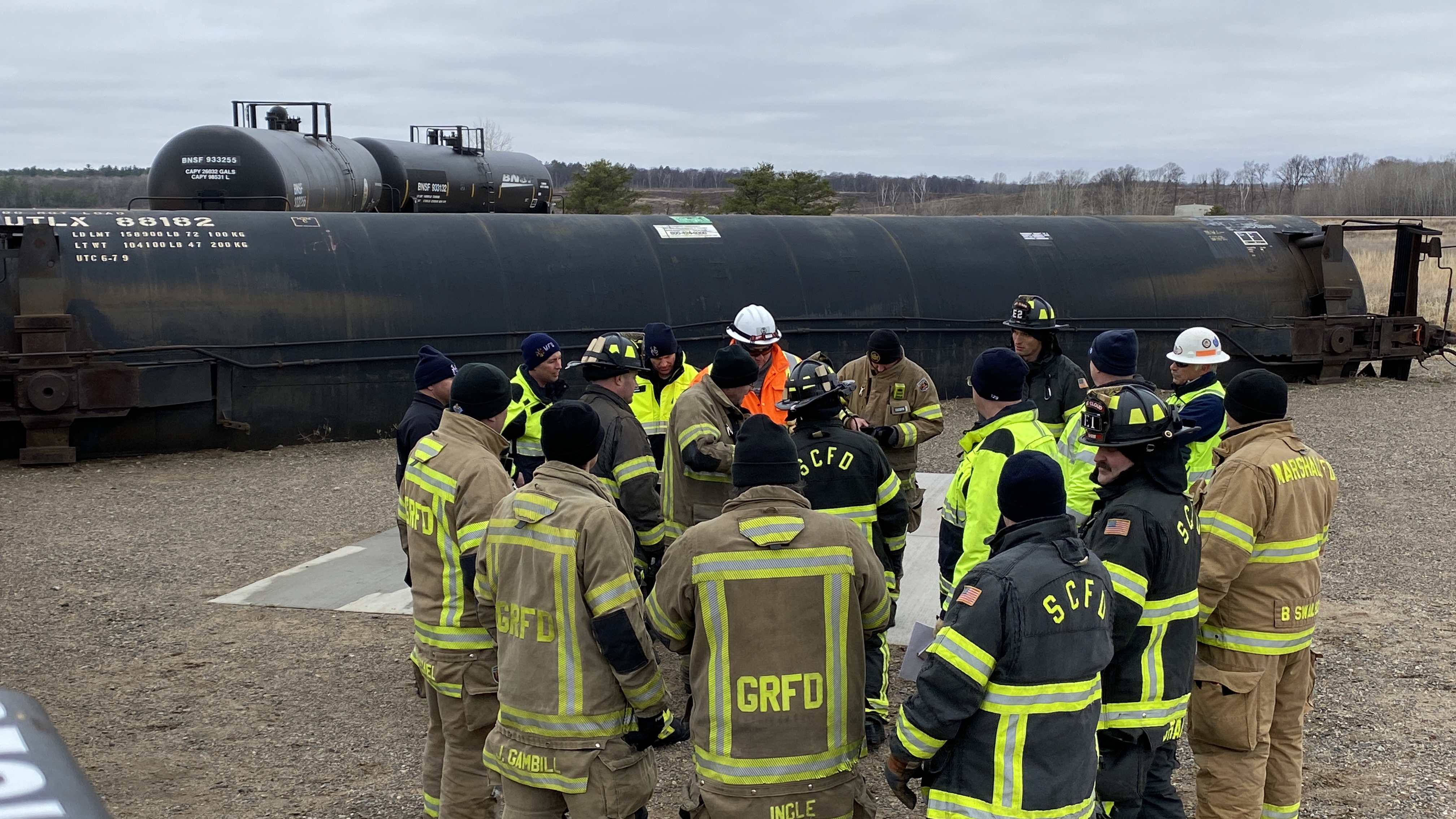 Firefighters stand near a turned over rail car. 