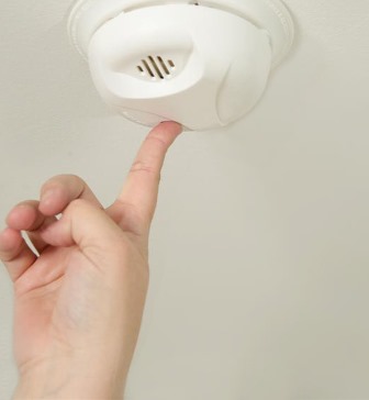 A person pushes the test button on a smoke alarm. 