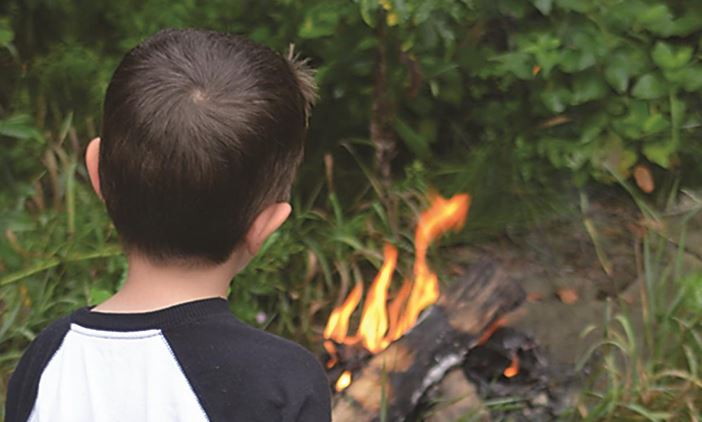 A child stares at a bonfire.